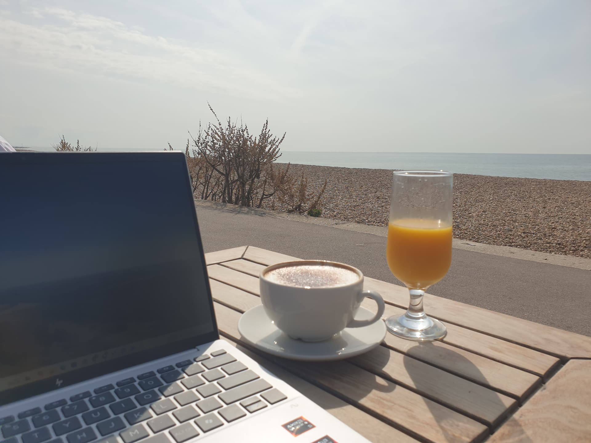 A laptop and coffee on a table overlooking the beach, ready for online learning and support